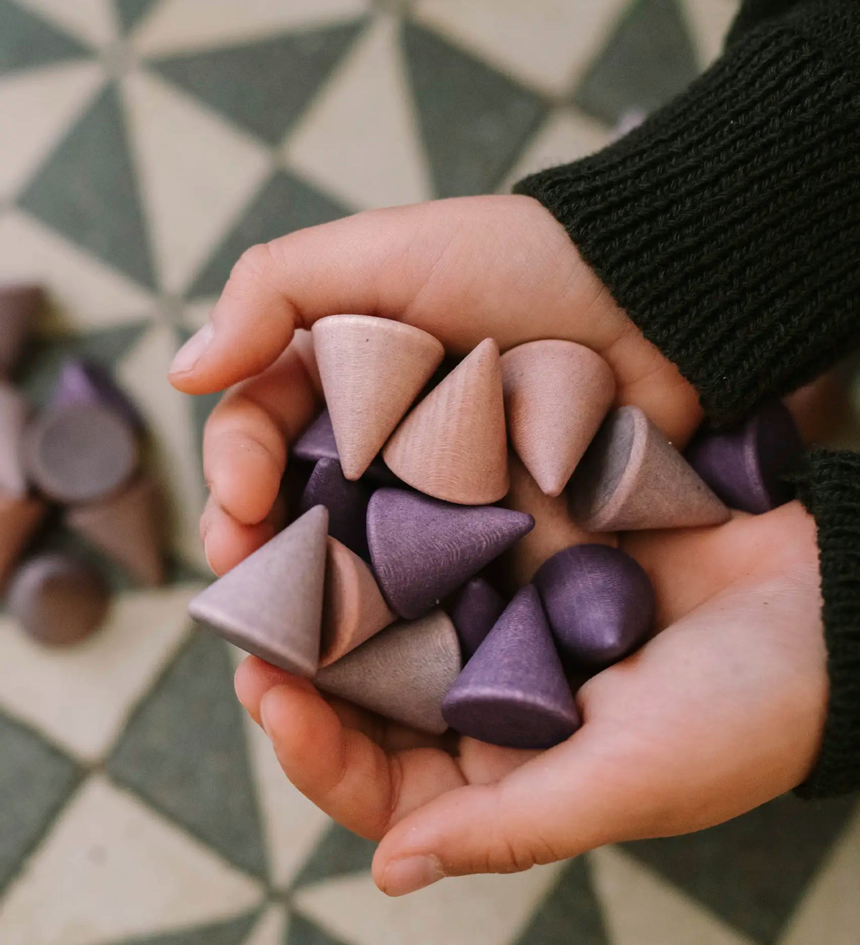 Close up of child hands holding the small Grapat handcrafted wooden purple mandala peak pieces. Each piece cone shaped