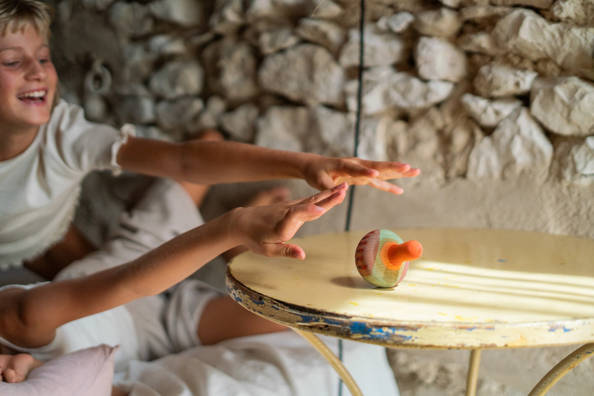 2 children playing with the Grapat wooden mellow wobbly orange bird on a wooden table next to a stone wall