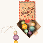 A red and blue striped cardboard box for the snow buddy wooden Grapat decorations on a cream background.