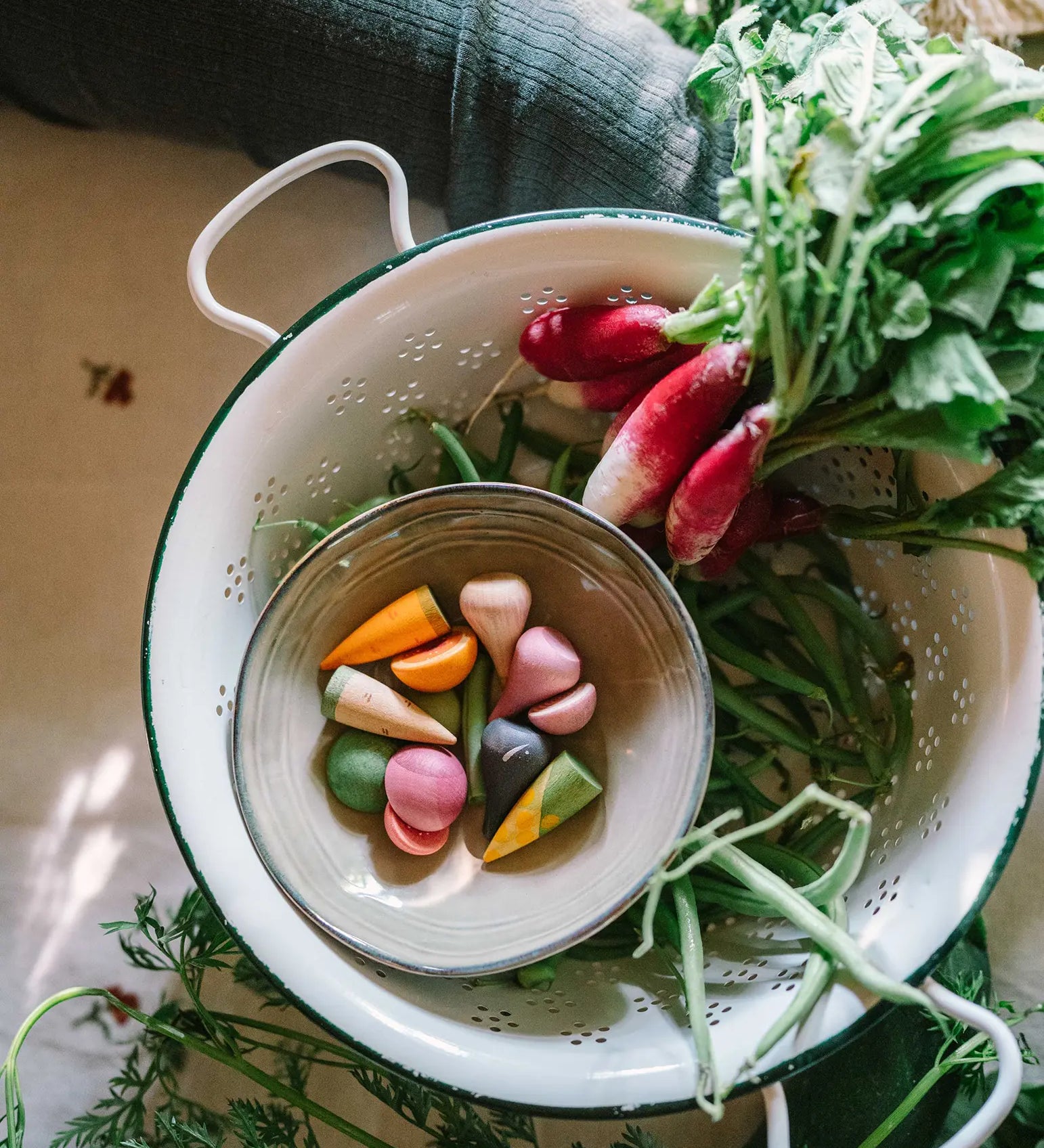 Grapat wooden veggie pieces in a bowl sitting in a colander filled with different veg. Each wooden piece is hand crafted and hand painted. 