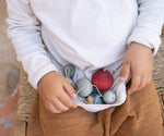 A top down photo of a child wild all 5 Grapat handmade and hand painted wooden wish balls on their lap. Hanging decorations available at Babipur.