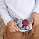 A top down photo of a child wild all 5 Grapat handmade and hand painted wooden wish balls on their lap. Hanging decorations available at Babipur.