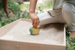 Child holding the Grapat wooden yellow flowing bird in a Grapat wooden freeplay set filled with sand. Showing the hand painted blue and green feathers