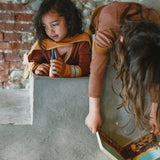 A child playing with the handmade and hand painted wooden nin peg doll on top of a stone surface from the Grapat advent calendar 2025 available at Babipur.