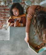 A child playing with the handmade and hand painted wooden nin peg doll on top of a stone surface from the Grapat advent calendar 2025 available at Babipur.