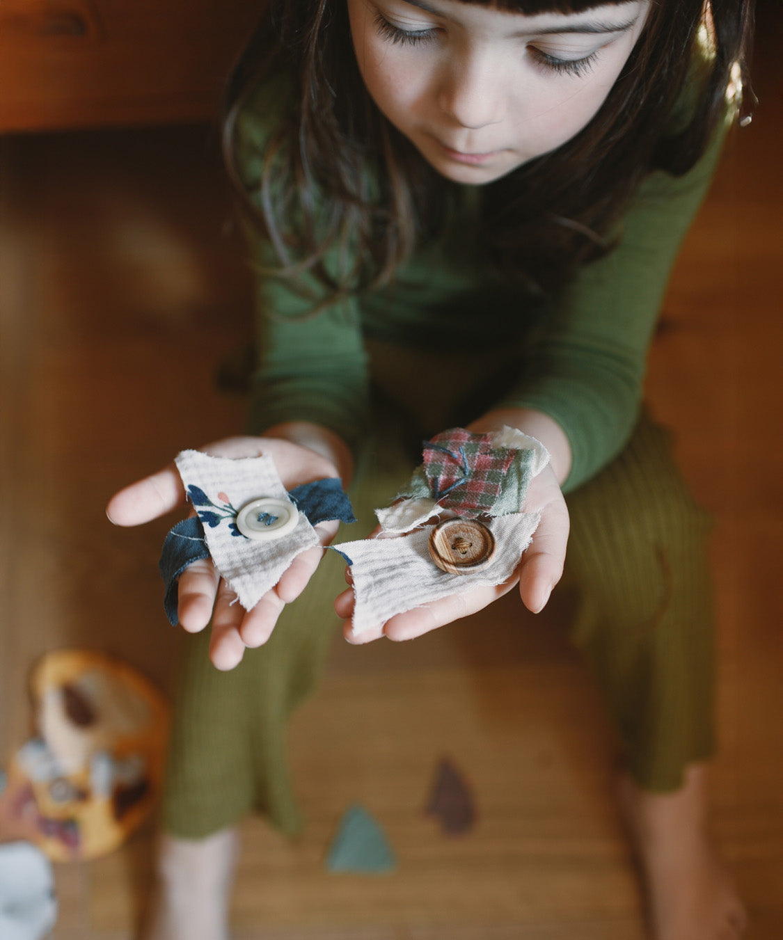 A child holding wooden and hand painted decorations made from wooden buttons pieces from the Grapat 2025 advent calendar available at Babipur