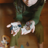 A child holding wooden and hand painted decorations made from wooden buttons pieces from the Grapat 2025 advent calendar available at Babipur