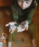 A child holding wooden and hand painted decorations made from wooden buttons pieces from the Grapat 2025 advent calendar available at Babipur