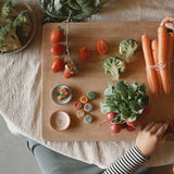 A top down view of a table with different veg and some of the handmade and hand painted wooden veg pieces from the Grapat advent 2025 calendar available at Babipur.