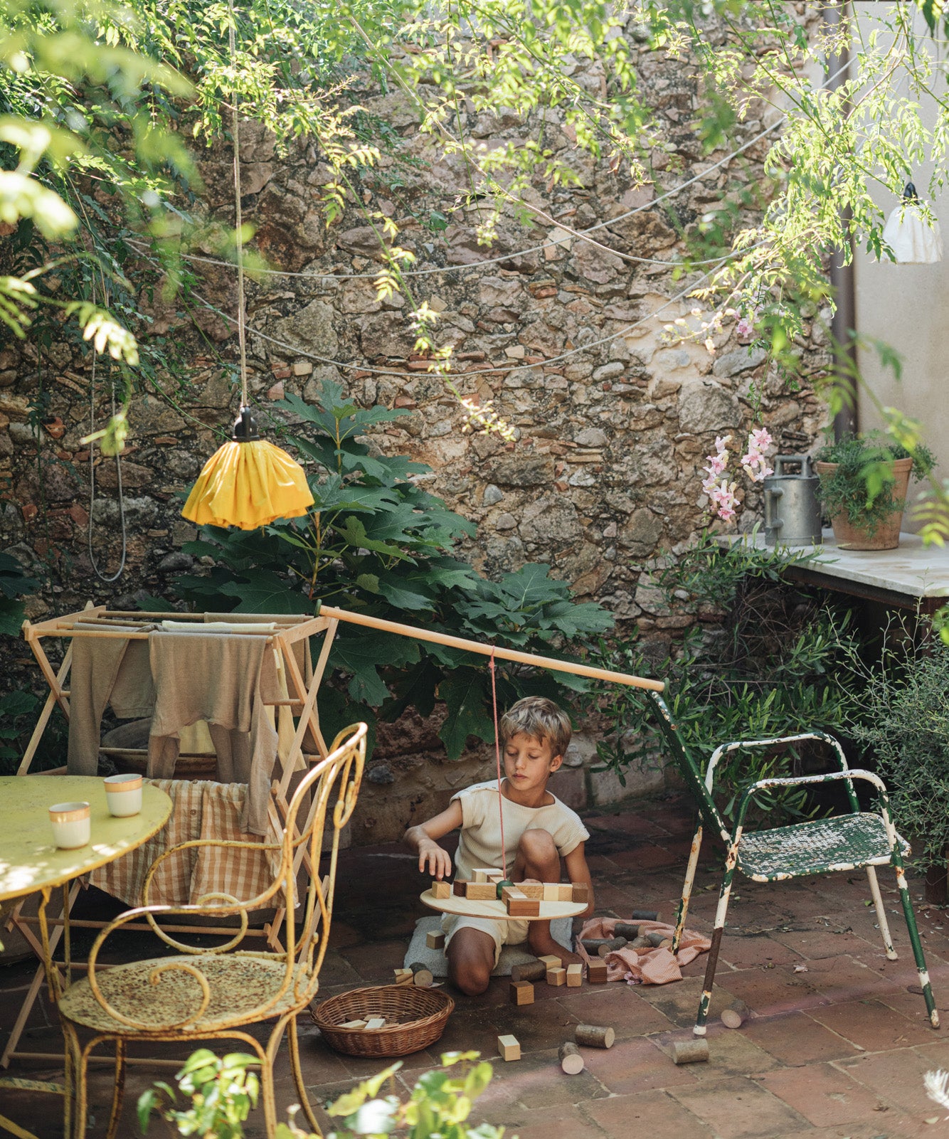 A child sitting outside playing with the Grapat wooden pendulum set balancing on a wooden clothes horse and garden chair with the different handcrafted wooden blocks balancing on the wooden board and scattered on the stone floor.