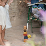Child playing outside on a wooden floor with the Grapat wooden serendipity set used as a stack. Features a brown, light pink, blue yellow orange and striped pieces. 
