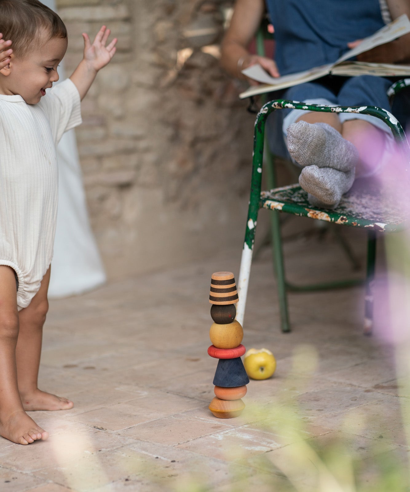 Child playing outside on a wooden floor with the Grapat wooden serendipity set used as a stack. Features a brown, light pink, blue yellow orange and striped pieces. 