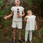 2 children standing on a grassy floor in the garden holding the pieces from the Grapat wooden serendipity stacking set. Features a brown, light pink, blue yellow orange and striped pieces. 