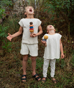 2 children standing on a grassy floor in the garden holding the pieces from the Grapat wooden serendipity stacking set. Features a brown, light pink, blue yellow orange and striped pieces. 