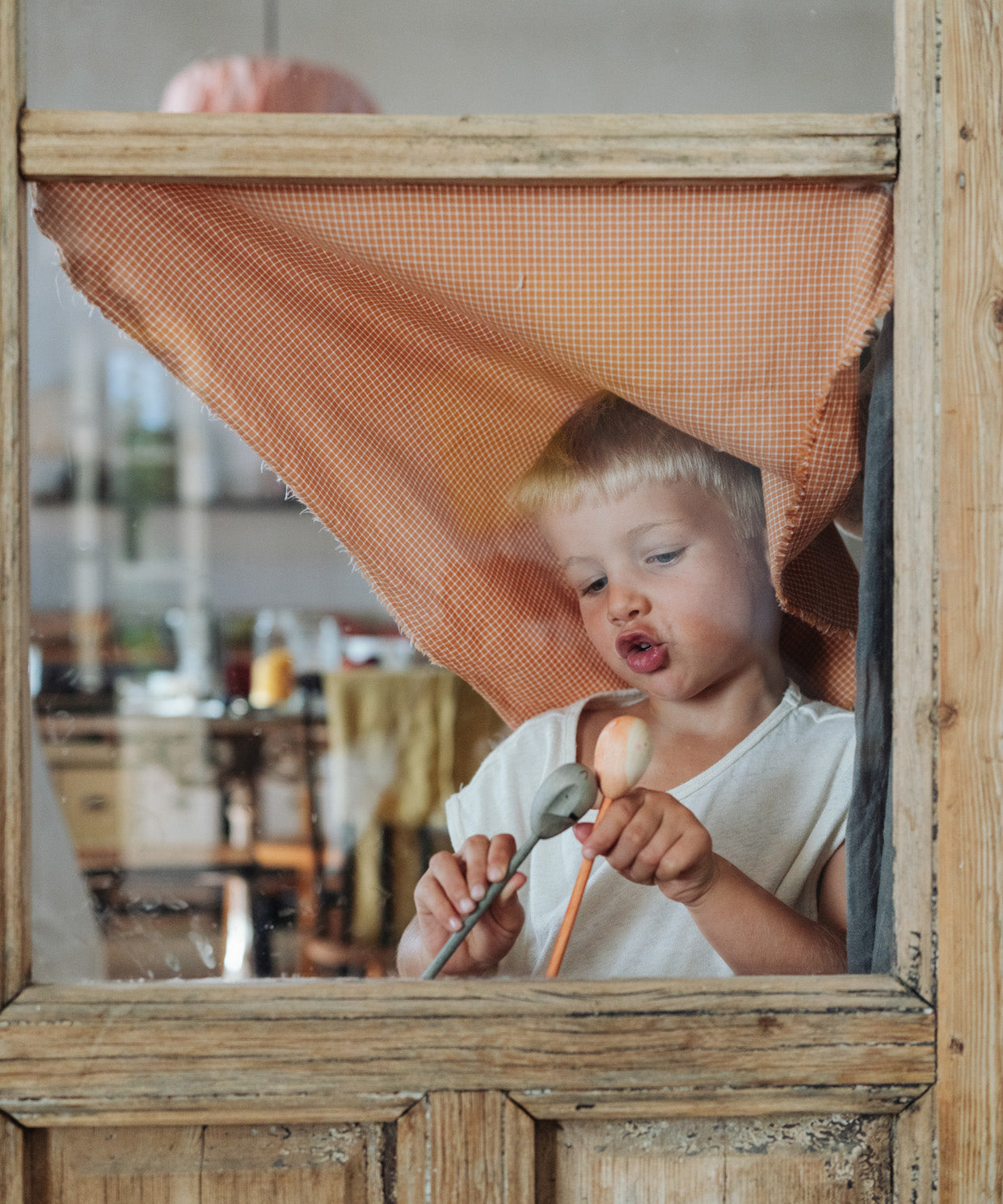 Child standing behind the wooden window frame playing with the grey bear puppet and the orange fox puppet. 