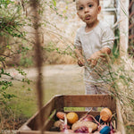 Child playing in the garden with pieces of the Grapat serendipity wooden stacking set placed in a wooden tray on a grassy floor