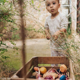 Child playing in the garden with pieces of the Grapat serendipity wooden stacking set placed in a wooden tray on a grassy floor