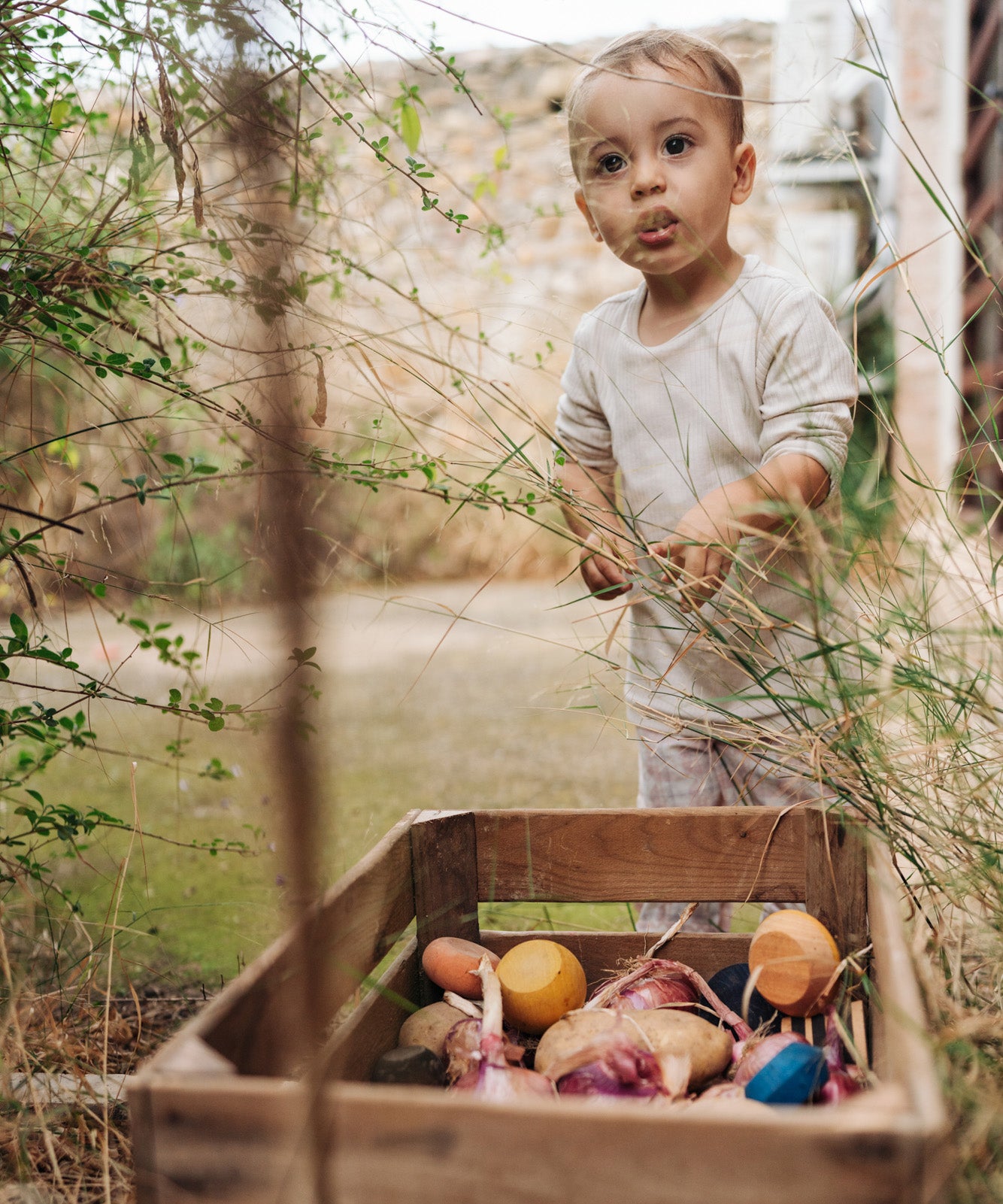 Child playing in the garden with pieces of the Grapat serendipity wooden stacking set placed in a wooden tray on a grassy floor