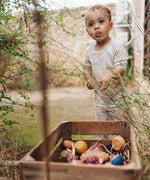 Child playing in the garden with pieces of the Grapat serendipity wooden stacking set placed in a wooden tray on a grassy floor