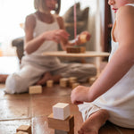 Child playing with the Grapat wooden pendulum set on a terracotta floor with handcrafted wooden blocks stacked on the floor