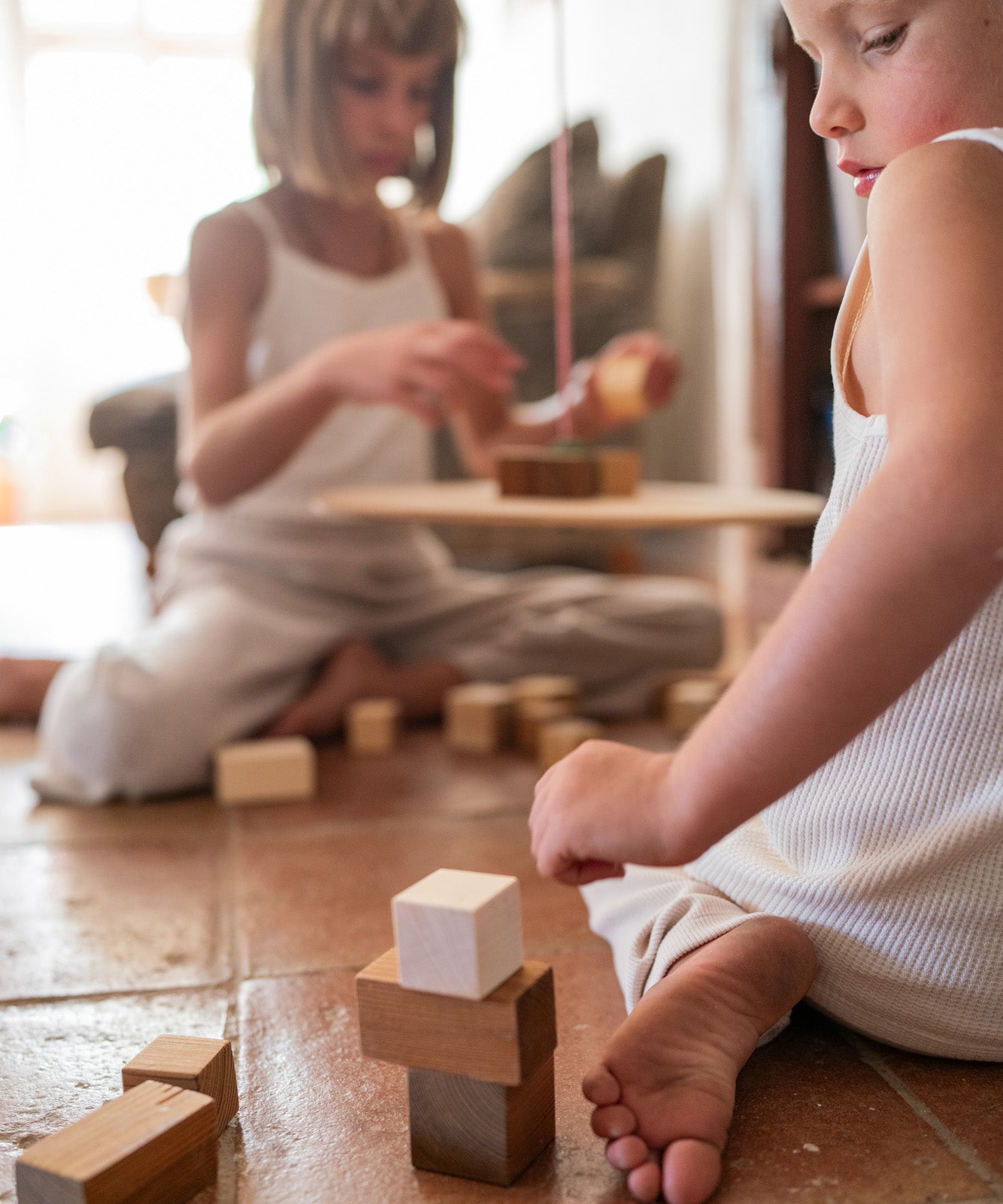 Child playing with the Grapat wooden pendulum set on a terracotta floor with handcrafted wooden blocks stacked on the floor