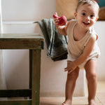 Child playing with the Grapat wooden pink chill wobbly bird next to a wooden table in the bathroom on a stone floor