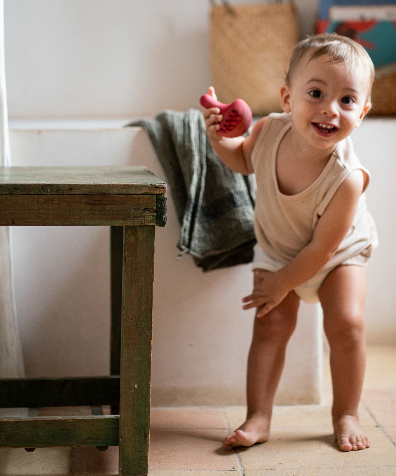 Child playing with the Grapat wooden pink chill wobbly bird next to a wooden table in the bathroom on a stone floor
