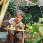 Child playing in the garden with the Grapat wooden pendulum set resting on a garden chair and wooden clothes horse. Showing the handcrafted wooden blocks balancing on the balance board and scattered on the stone floor.