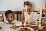 2 children sitting next to a wooden table stacking the handcrafted Grapat wooden tubes and planks. A close up showing the different painted tubes featuring flowers, windows and ladders. 