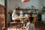 Child sitting next to a kitchen table playing with the Grapat wooden twin soul puppets with 2 puppets on the wooden stand