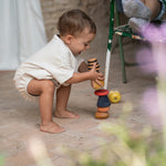Child outside stacking the pieces from the Grapat serendipity on a stone floor. Features a brown, light pink, blue yellow orange and striped pieces. 