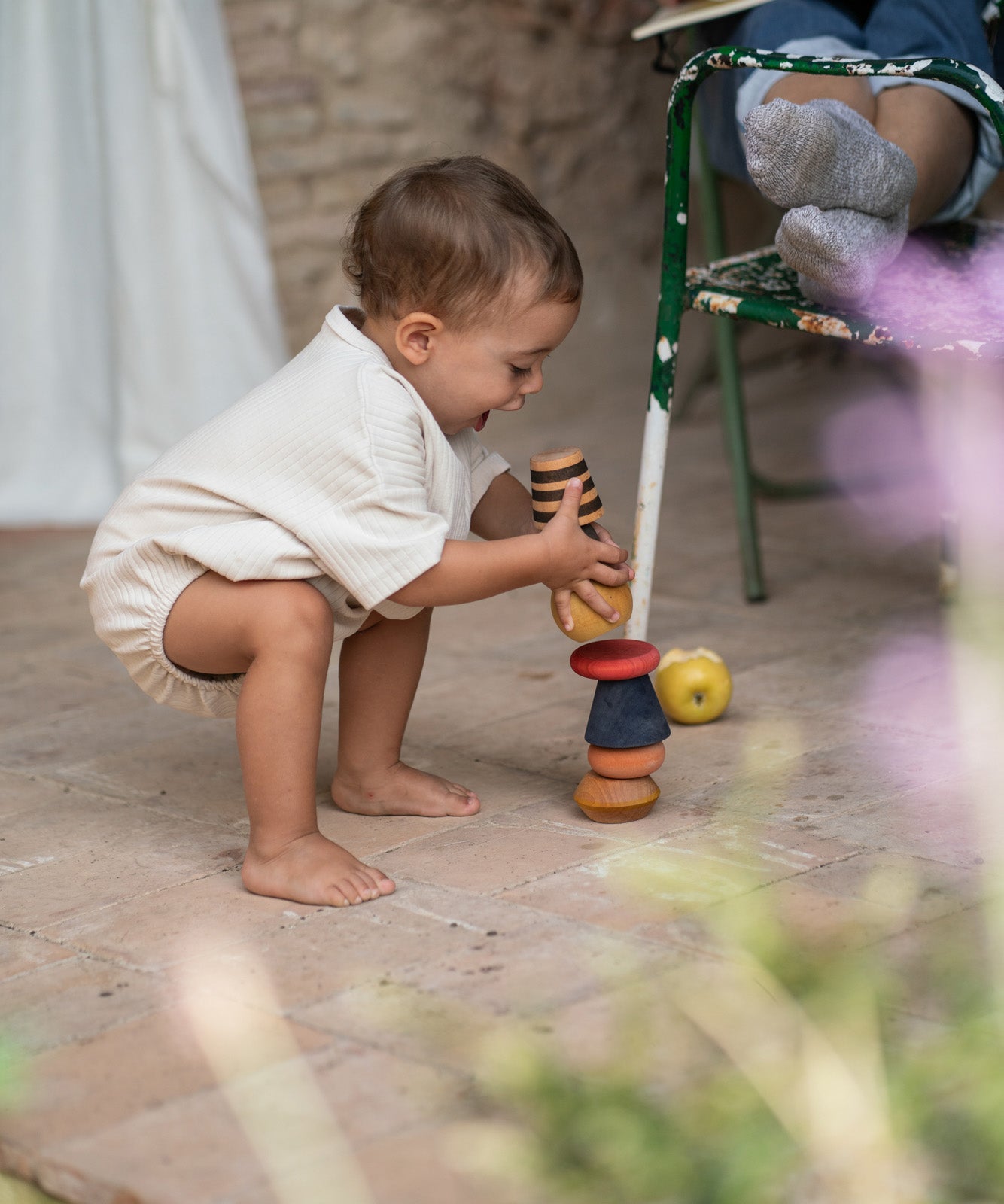 Child outside stacking the pieces from the Grapat serendipity on a stone floor. Features a brown, light pink, blue yellow orange and striped pieces. 