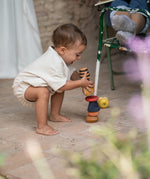 Child outside stacking the pieces from the Grapat serendipity on a stone floor. Features a brown, light pink, blue yellow orange and striped pieces. 