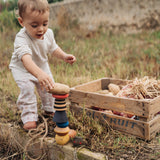 Child playing with the Grapat wooden serendipity stacking set in the garden Showing the different handcrafted tactile pieces stacked on the grass and a potato placed on top of the stack