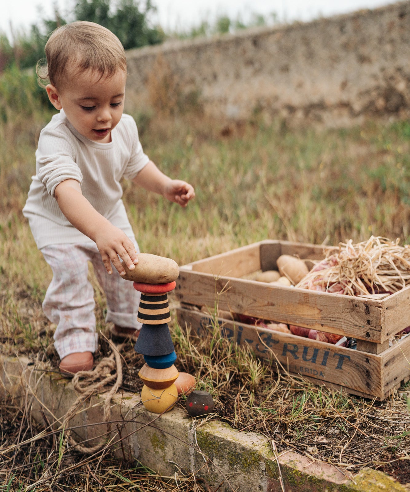 Child playing with the Grapat wooden serendipity stacking set in the garden Showing the different handcrafted tactile pieces stacked on the grass and a potato placed on top of the stack