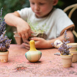 Child sorting out plants on a garden table with the Grapat wooden yellow flowing bird resting on the table next to small plants