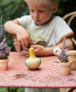 Child sorting out plants on a garden table with the Grapat wooden yellow flowing bird resting on the table next to small plants