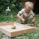 Child playing in the garden with the Grapat wooden flowing yellow bird sitting in the Grapat wooden freeplay tray filled with sand on a grassy floor. 