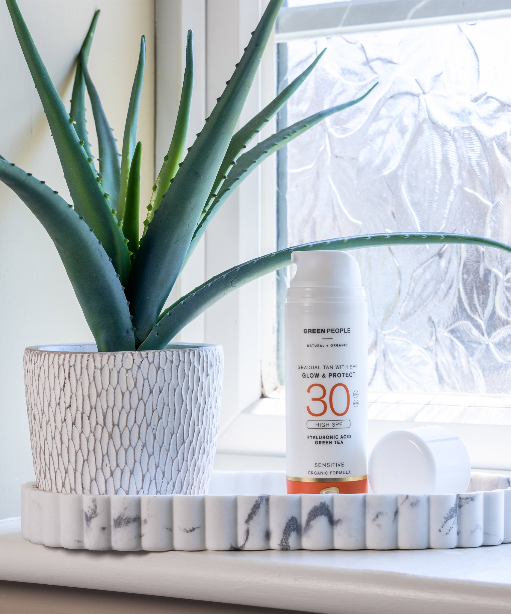 Green People glow & protect spf30 150ml cream bottle standing on a stone dish in a bathroom next to a aloe vera plant 