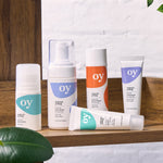 The full collection of the OY! Organic Young skincare range which includes deodorant, face wash, moisturiser, concealer and serum. All the items are stood on a wooden shelf, with a white backgorund