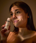 A person holding the Green People Age Defy+ Daily SPF30 Moisturiser next to their face, whilst the sun lights up their face and neck