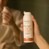 A close up of an adult's hand holding the Green People glow & protect spf30 150ml cream