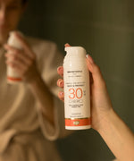 A close up of an adult's hand holding the Green People glow & protect spf30 150ml cream
