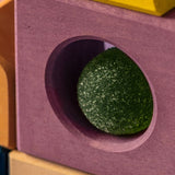 Close up of a purple tactile piece from the Grimm's wooden panorama building set, shows hand carved hole detail and green ball sitting inside 