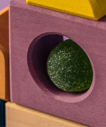 Close up of a purple tactile piece from the Grimm's wooden panorama building set, shows hand carved hole detail and green ball sitting inside 