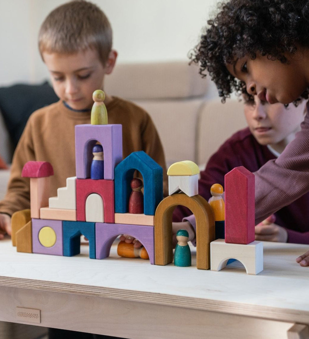 Children playing with the Grimm's wooden panorama building set on a wooden table in a living room setting