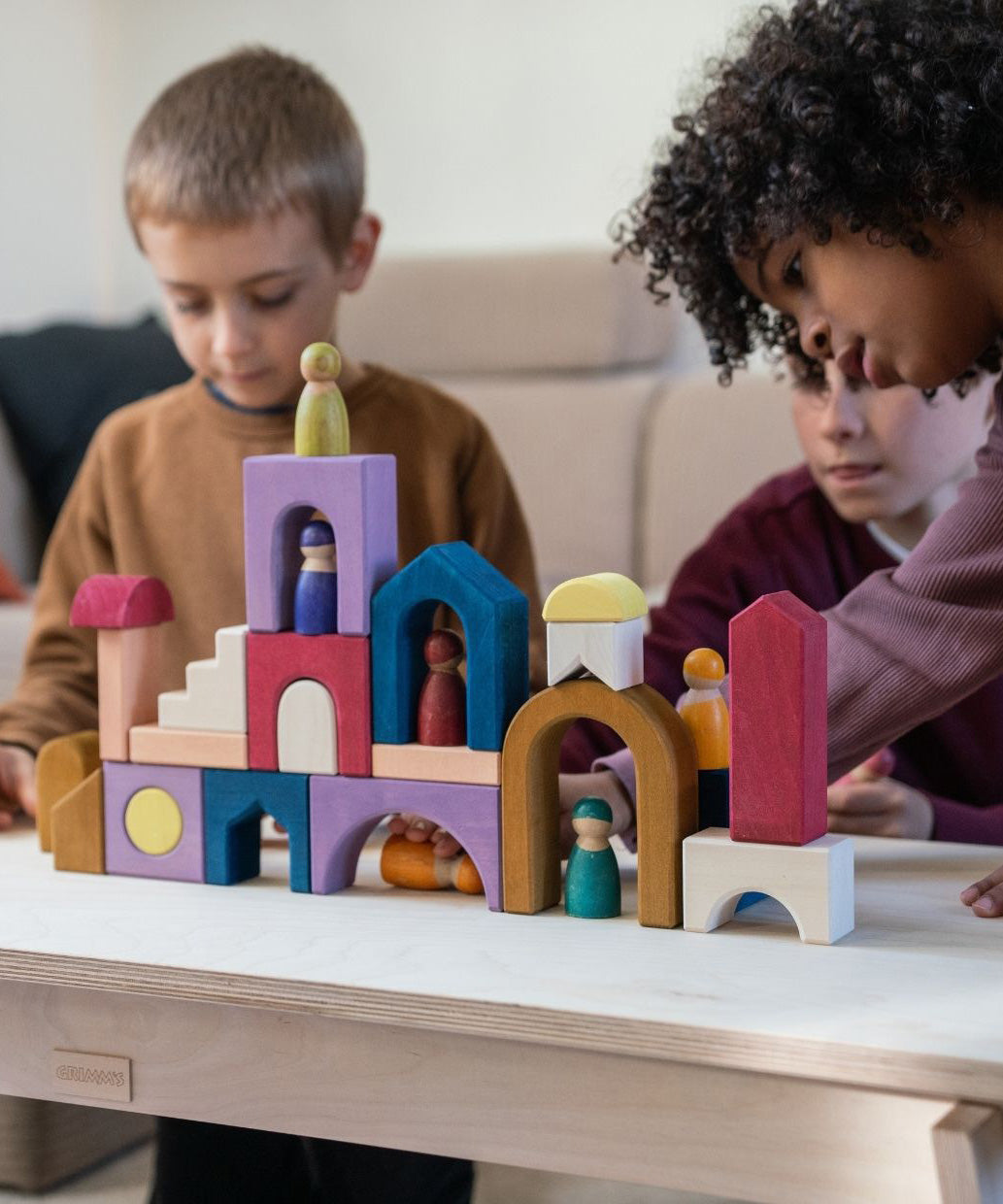Children playing with the Grimm's wooden panorama building set on a wooden table in a living room setting