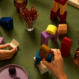 Adult hand stacking Grimms panorama wooden tactile pieces on a green cloth 