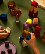 Adult hand stacking Grimms panorama wooden tactile pieces on a green cloth 
