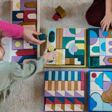 Grimm's wooden panorama building set inside the rectangle frame next to other building sets lying flat on a fluffy carpet